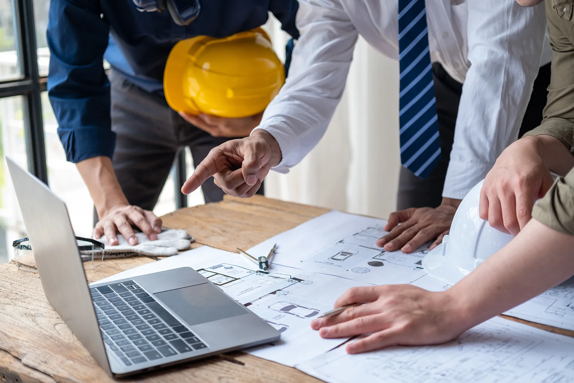 Three workers with a yellow hard hat looking and pointing at a computer